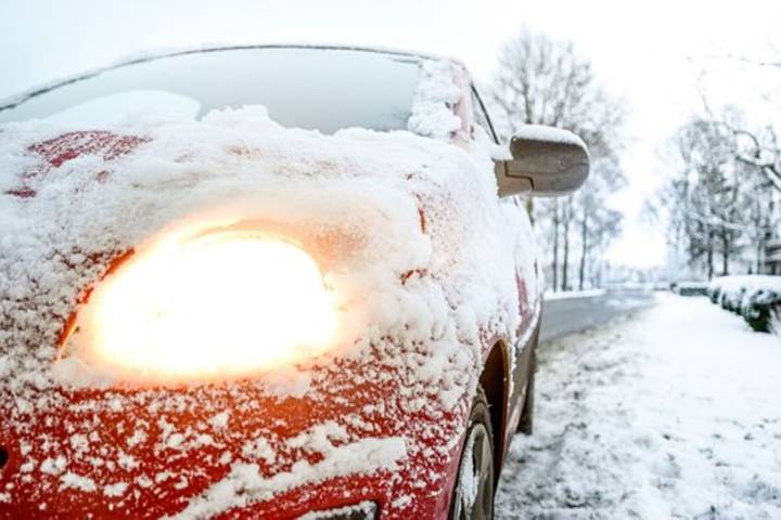 Voiture rouge couverte de neige, phare avant à moitié déneigé et allumé