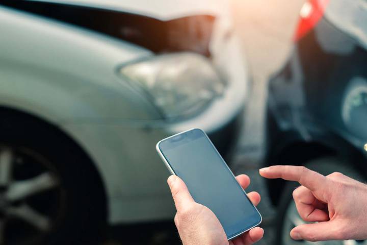 Des mains tiennent un téléphone devant deux voitures accidentées