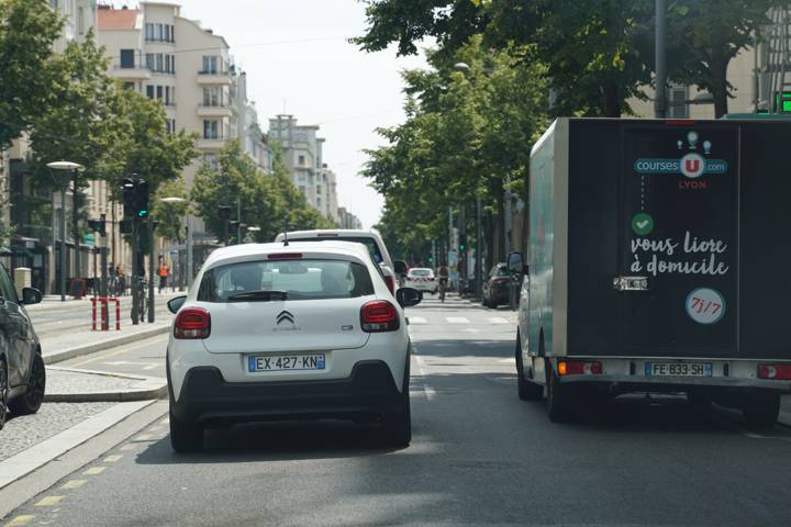Rue de ville, une voiture blanche suit un camion de livraison entre les immeubles