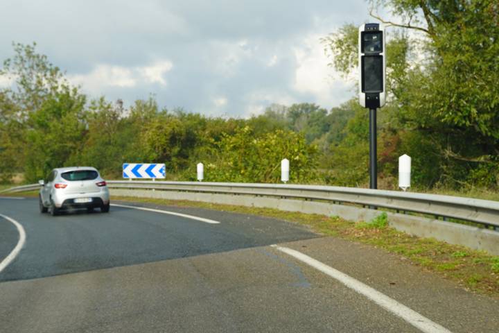 Radar fixe sur un poteau au bord d'une route de campagne, une voiture approche du virage