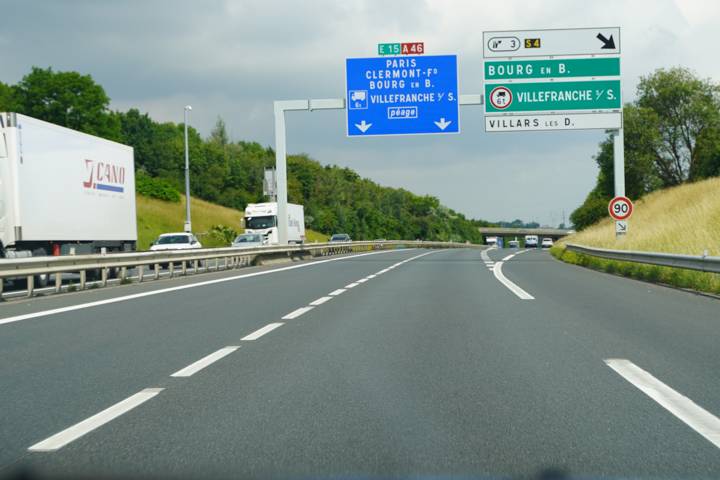 Voie rapide avec panneaux de direction verts et bleus vers Villefranche, un camion à gauche