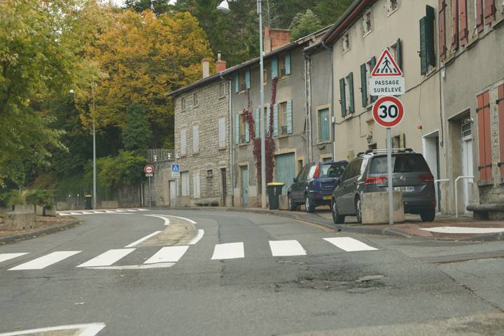 Rue de village avec un passage surélevé limité à 30 km/h et des voitures stationnées