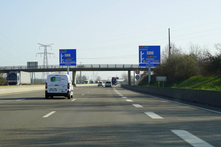 Autoroute à plusieurs voies avec panneaux bleus vers Genève et Grenoble, un fourgon devant