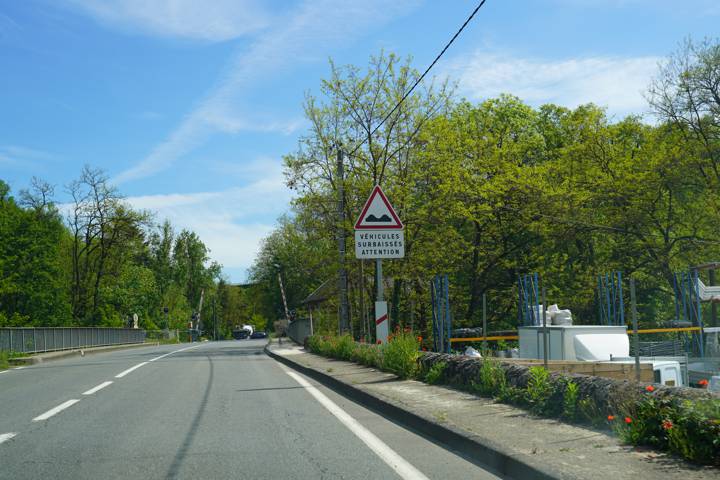 Route bordée d'arbres approchant un passage à niveau, panneau triangulaire de danger