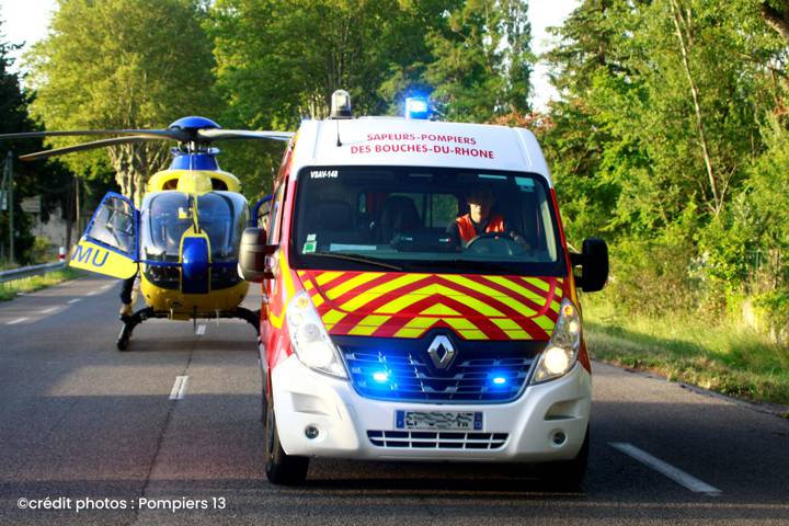 Camion de pompiers et hélicoptère du SAMU, gyrophares bleus allumés, sur une route