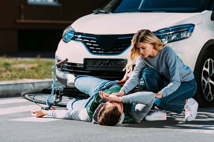 Cycliste à terre après un accident, une femme se penche pour le secourir devant une voiture