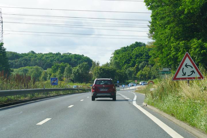 Route de campagne, voiture rouge, panneau triangulaire annonçant un rond-point à droite