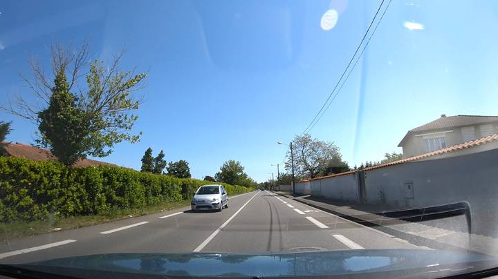 Route résidentielle avec une voiture blanche en sens inverse et une bande cyclable à droite