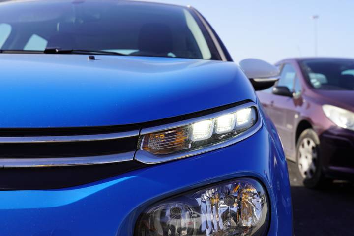 Gros plan sur l'avant d'une voiture bleue, optique de phare avant allumé