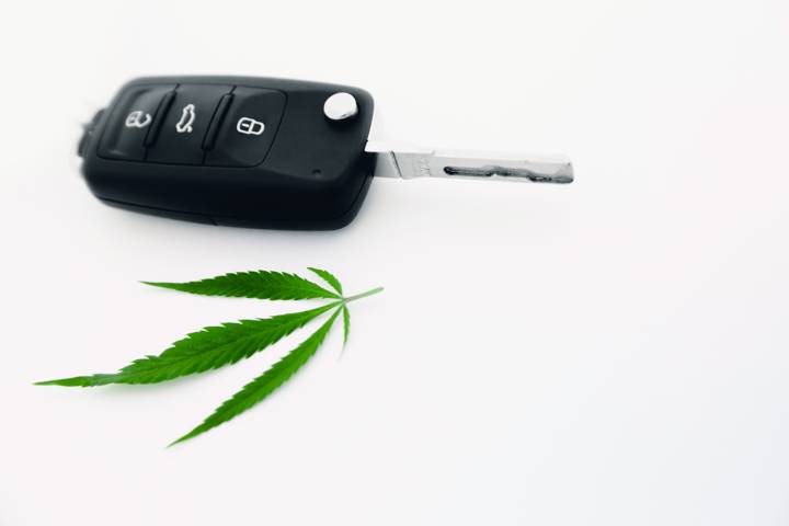 Clé de voiture posée à côté d'une feuille de cannabis sur fond blanc