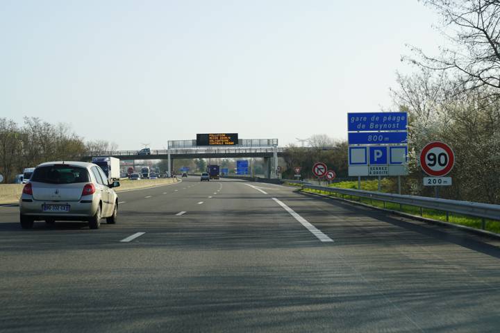 Voie rapide à l'approche d'une gare de péage avec un panneau de limitation à 90 km/h
