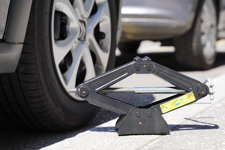 Cric placé au sol près d'une roue de voiture, prêt à soulever le véhicule